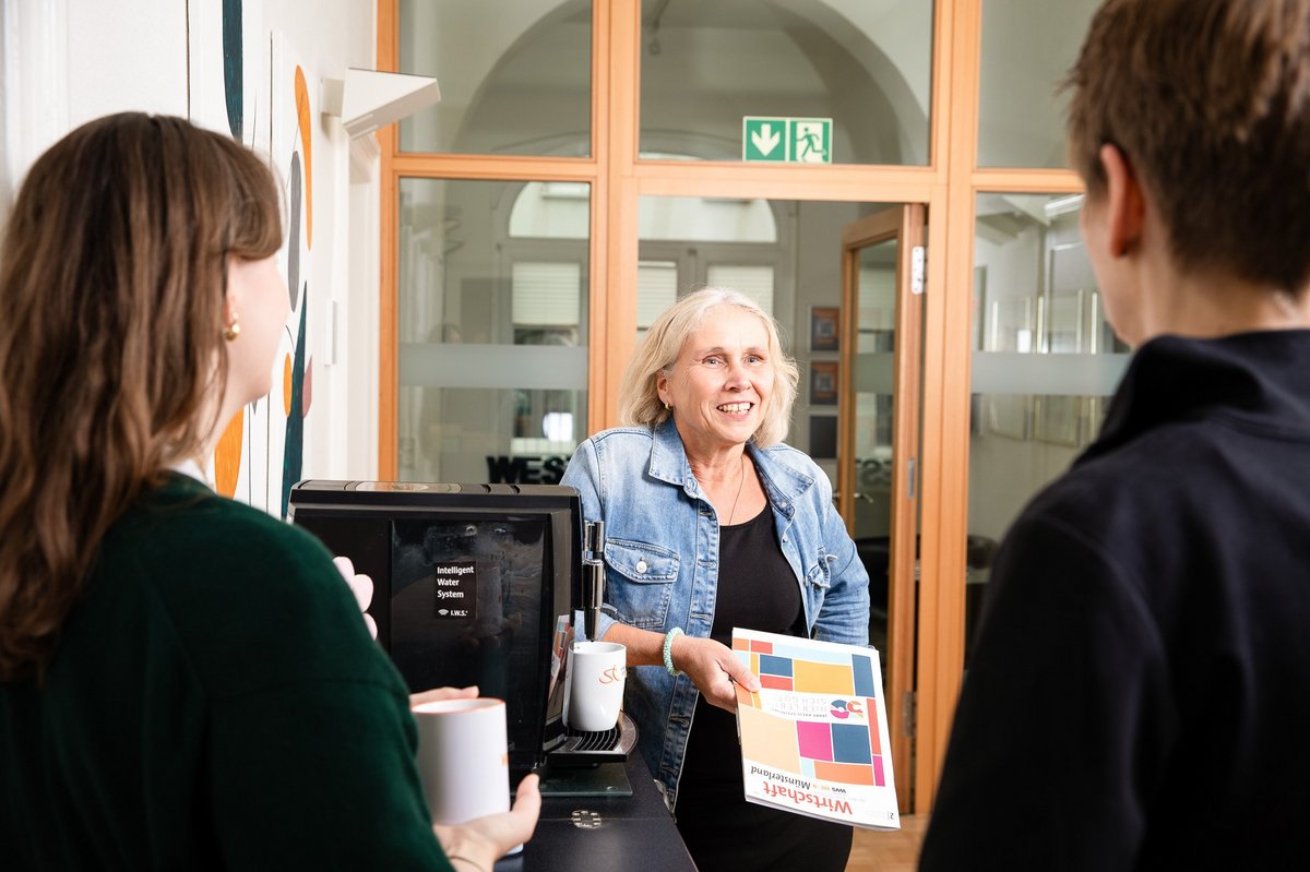 3 Personen stehen an einer Kaffeemaschine und unterhalten sich.